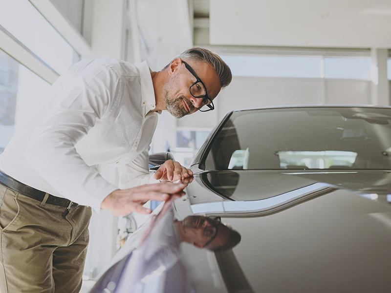 Mann begutachtet die geschlossene Motorhaube eines Autos: Unfallwagen erkennen